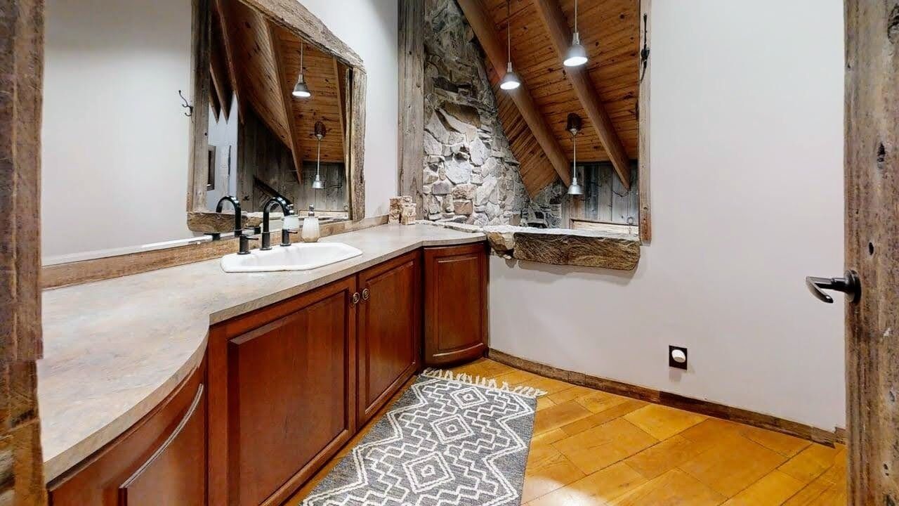 A bathroom with a stone wall, wooden ceiling beams, a large mirror, and a white sink.