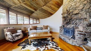 Un interior rústico con chimenea de piedra, techo de madera y alfombra de cuero de vaca.