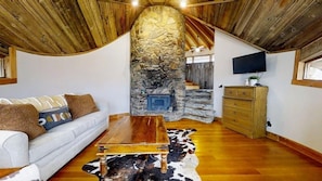 Ein gemütliches Wohnzimmer mit Kamin aus Stein, Holzboden und einem weißen Sofa.