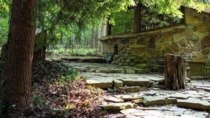 Un chemin de pierres mène à un bâtiment en pierre, lui-même entouré d’arbres.