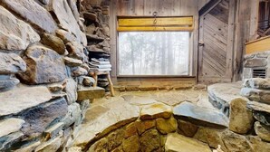 Une pièce aux murs de pierre, avec une fenêtre en bois donnant sur une forêt.