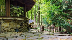 Un sentier de pierres mène à un chalet en bois doté d’un mur en pierre, le tout étant entouré d’une forêt.