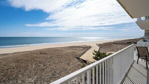 Blick auf einen Strand vom Balkon, mit weißer Brüstung, feinem Sand und dem Meer.