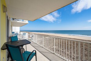 A balcony with a table and chairs, overlooking a beach with a fence and a clear sky. - New for 2025! Lovely 3 bedroom, 3 bath condo has a private balcony offering a spectacular ocean view (Ocean City)
