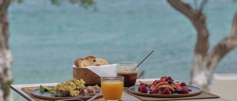A breakfast table with eggs, toast, fruit, and juice, overlooking a body of water.