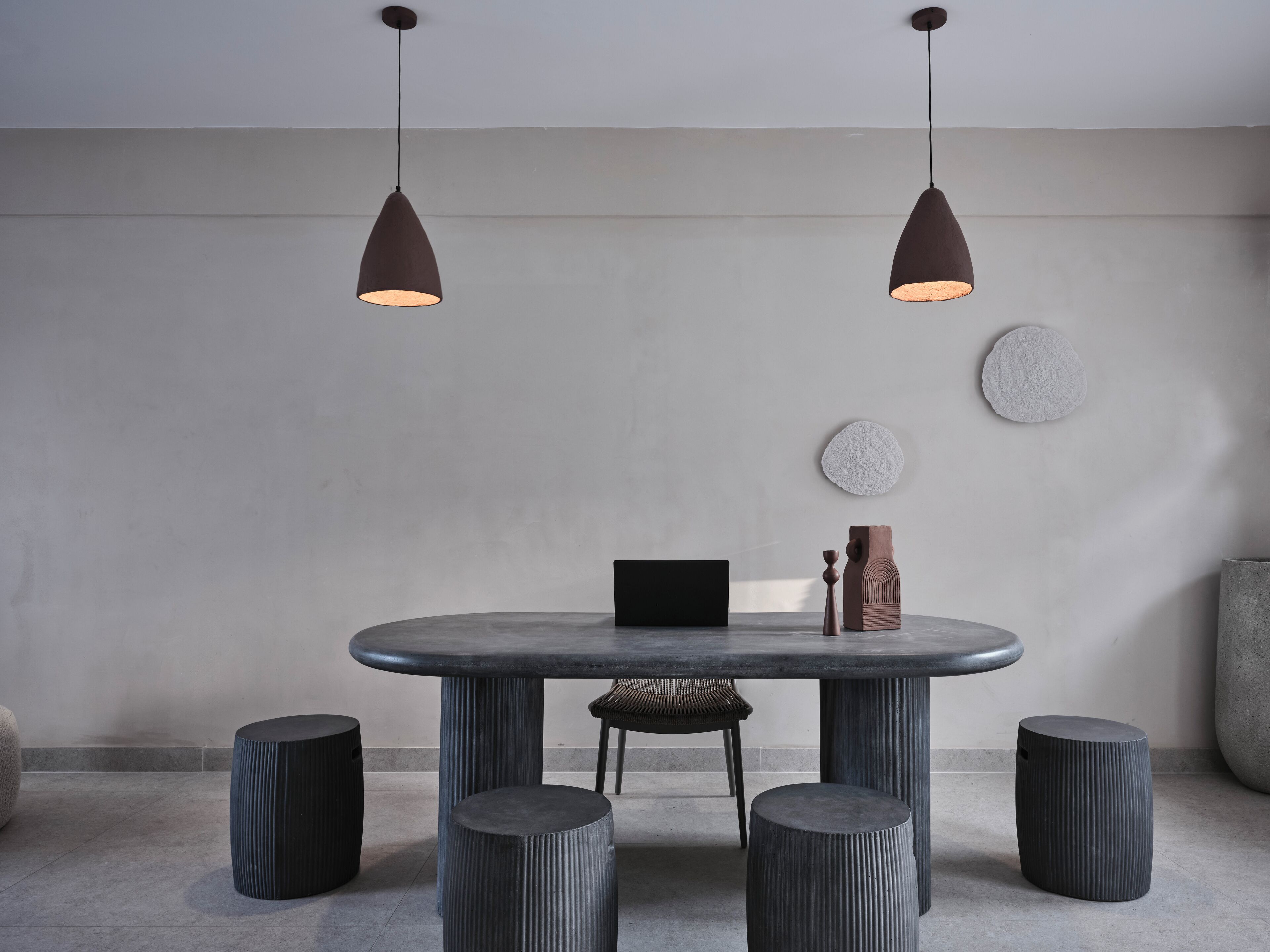 Un espace repas moderne avec une table ronde, deux lampes suspendues et six tabourets à l’assise striée.