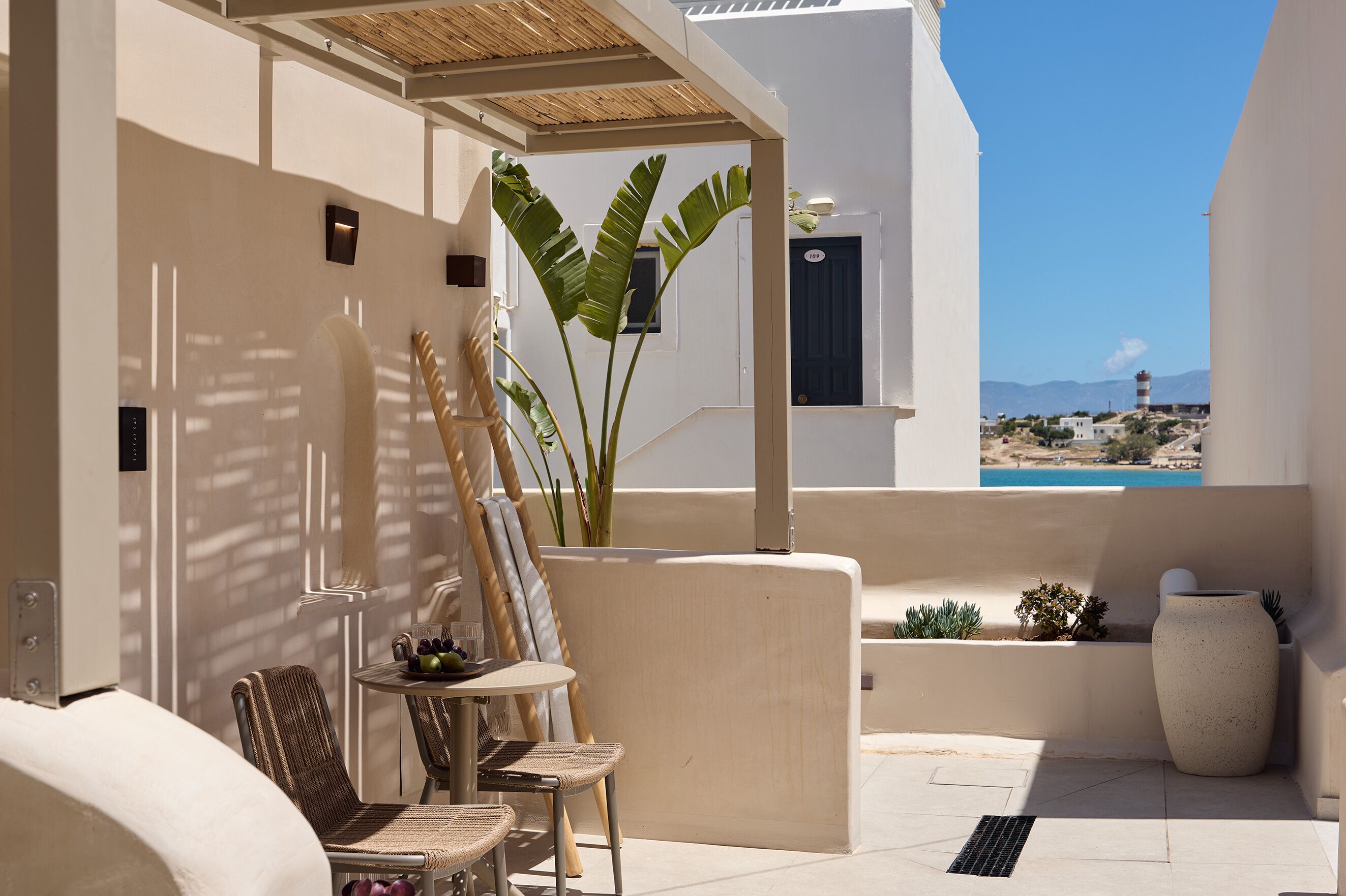 A sunlit outdoor seating area with a table, chairs, and a potted plant.