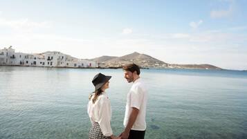 A couple holding hands by a body of water with white buildings in the background.