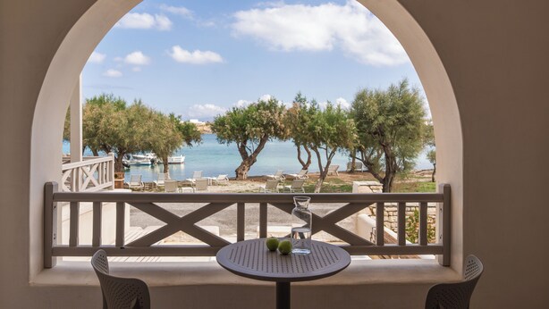 Un balcón con vistas al mar, árboles y una mesa con dos manzanas.