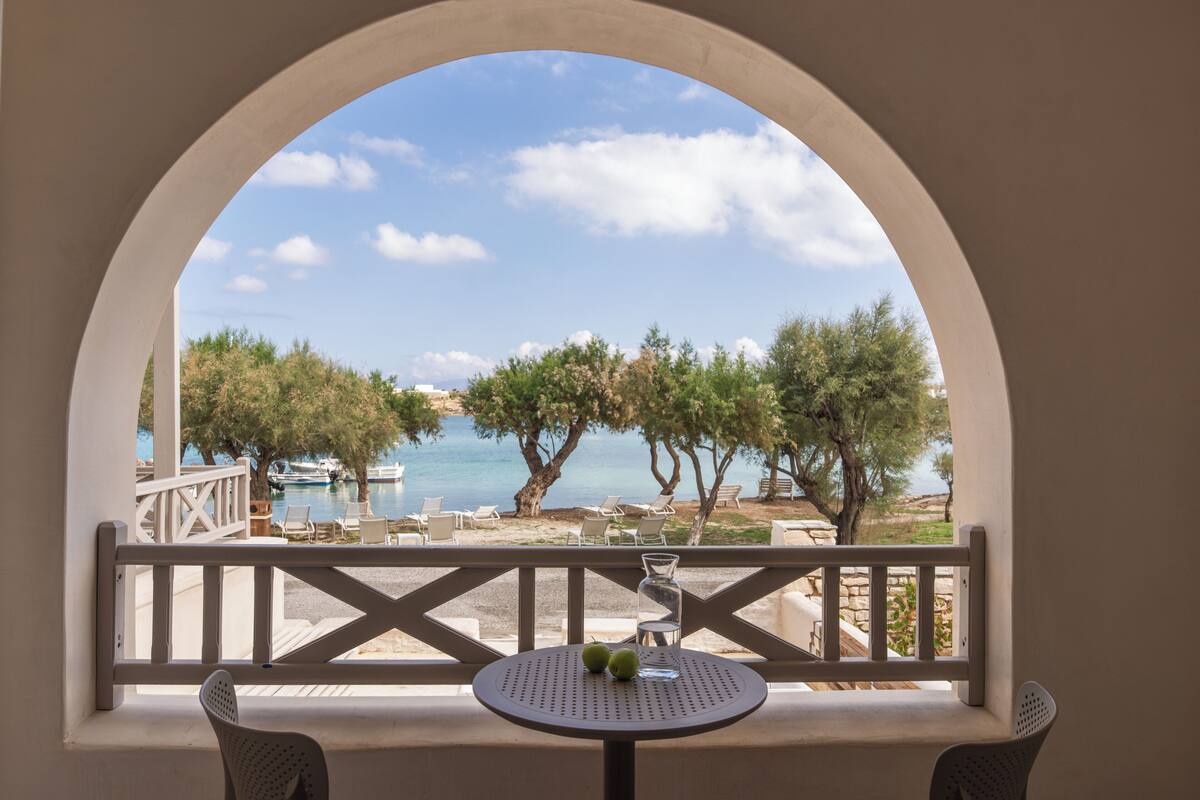 Varanda com vista para o mar, árvores e uma mesa com duas maçãs.