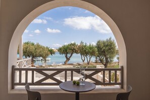 A balcony with a view of the sea, trees, and a table with two apples.