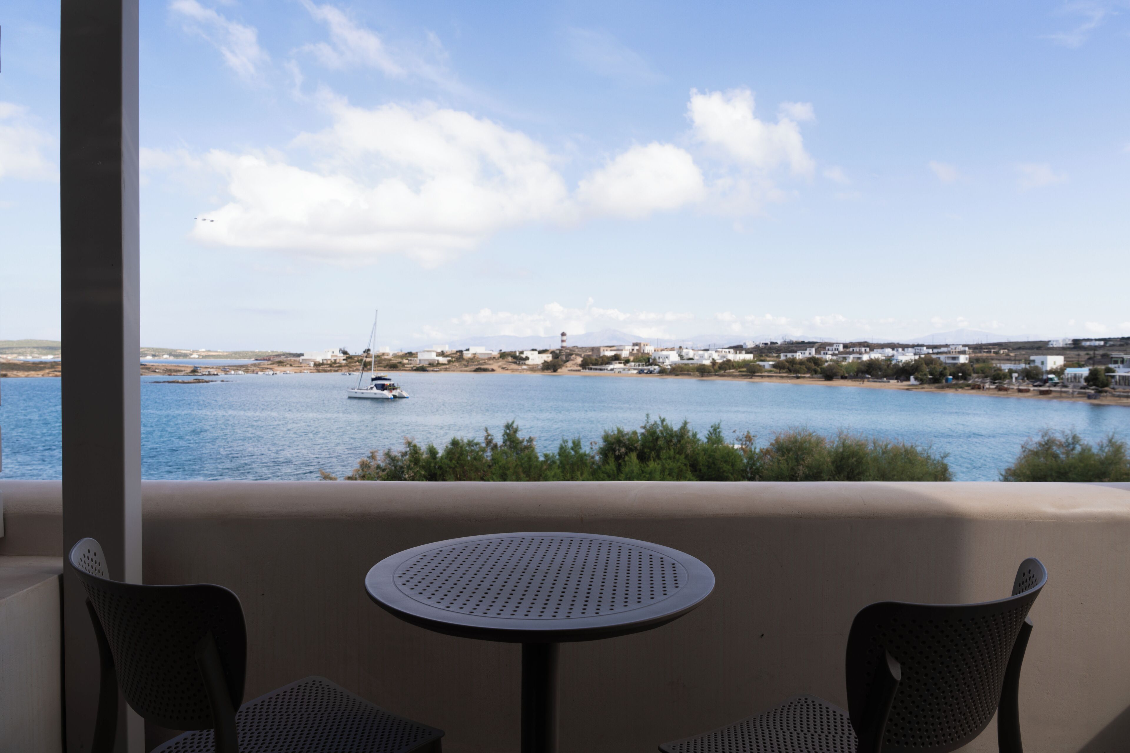 Un balcon avec une table ronde et deux chaises donnant sur une étendue d’eau où l’on aperçoit un voilier.