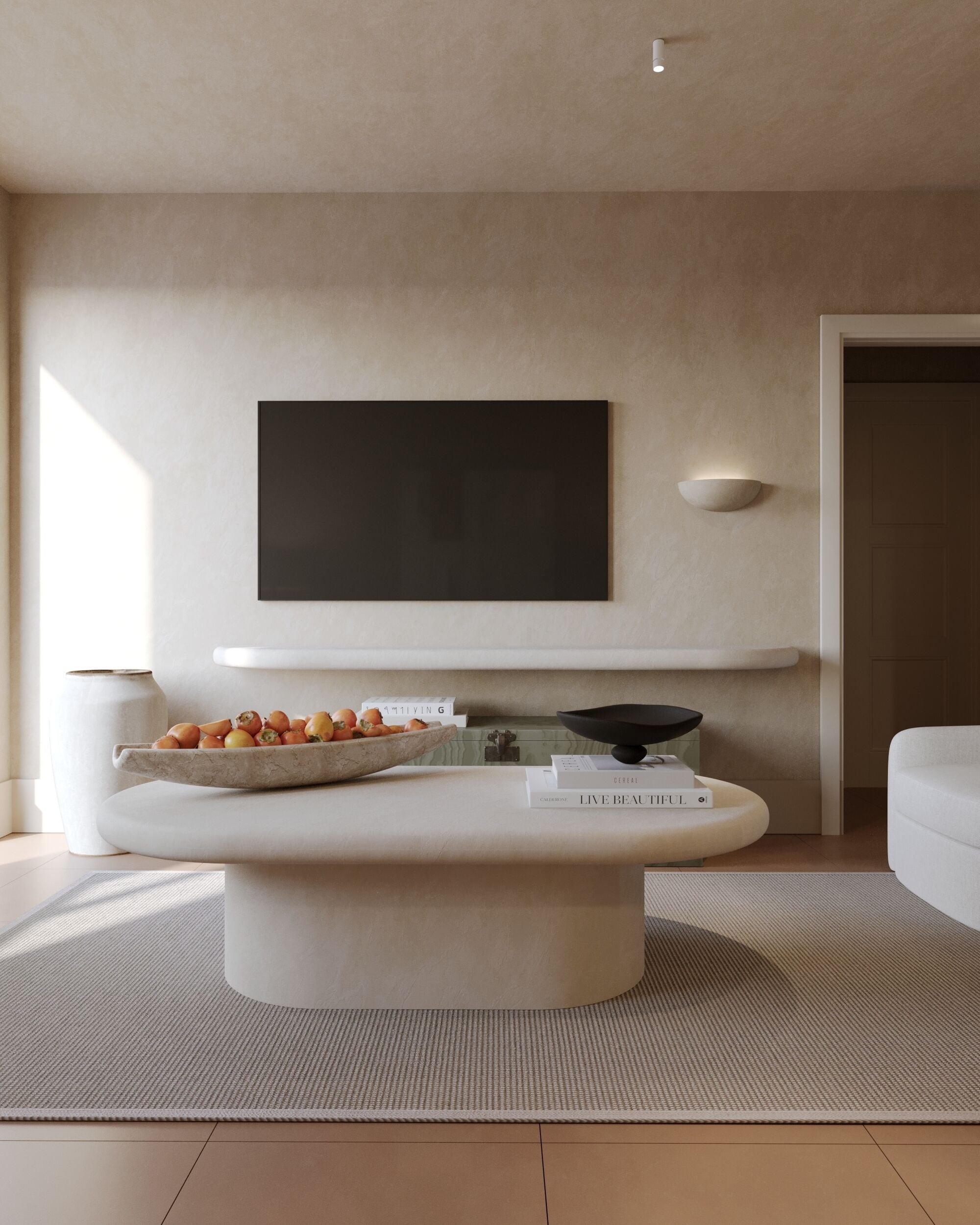 A modern living room with a large flat-screen TV mounted on the wall, a central island with a bowl of fruit, and a few books.