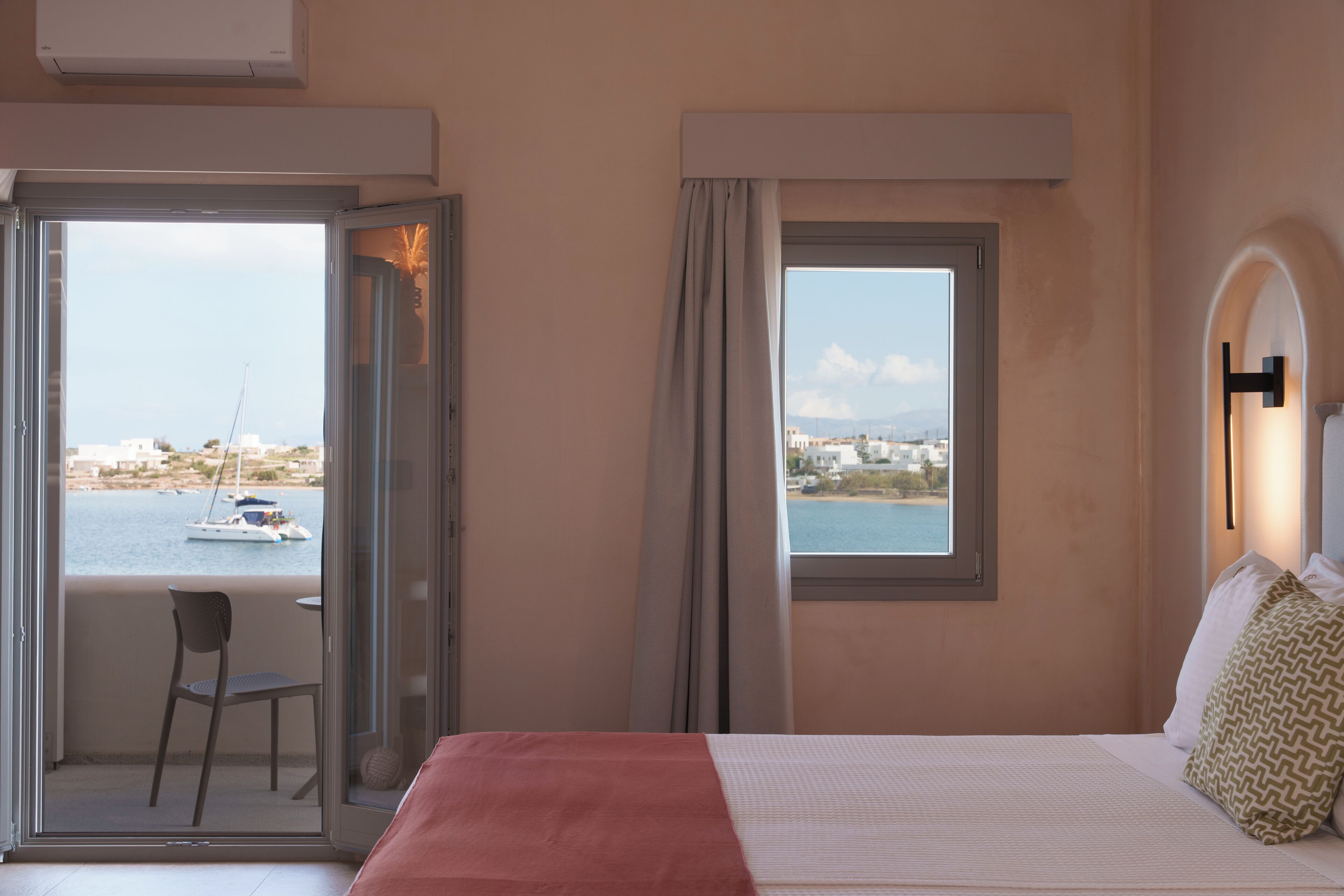 Habitación de hotel con cama, una silla, una mesa y vista al mar y barcos.
