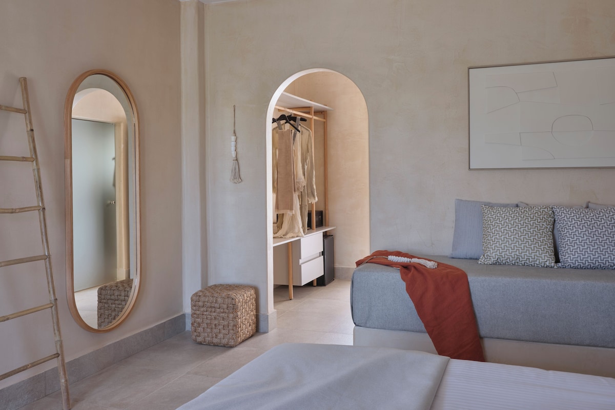 A modern bedroom with a bed, a grey sofa, a wardrobe, and a mirror.