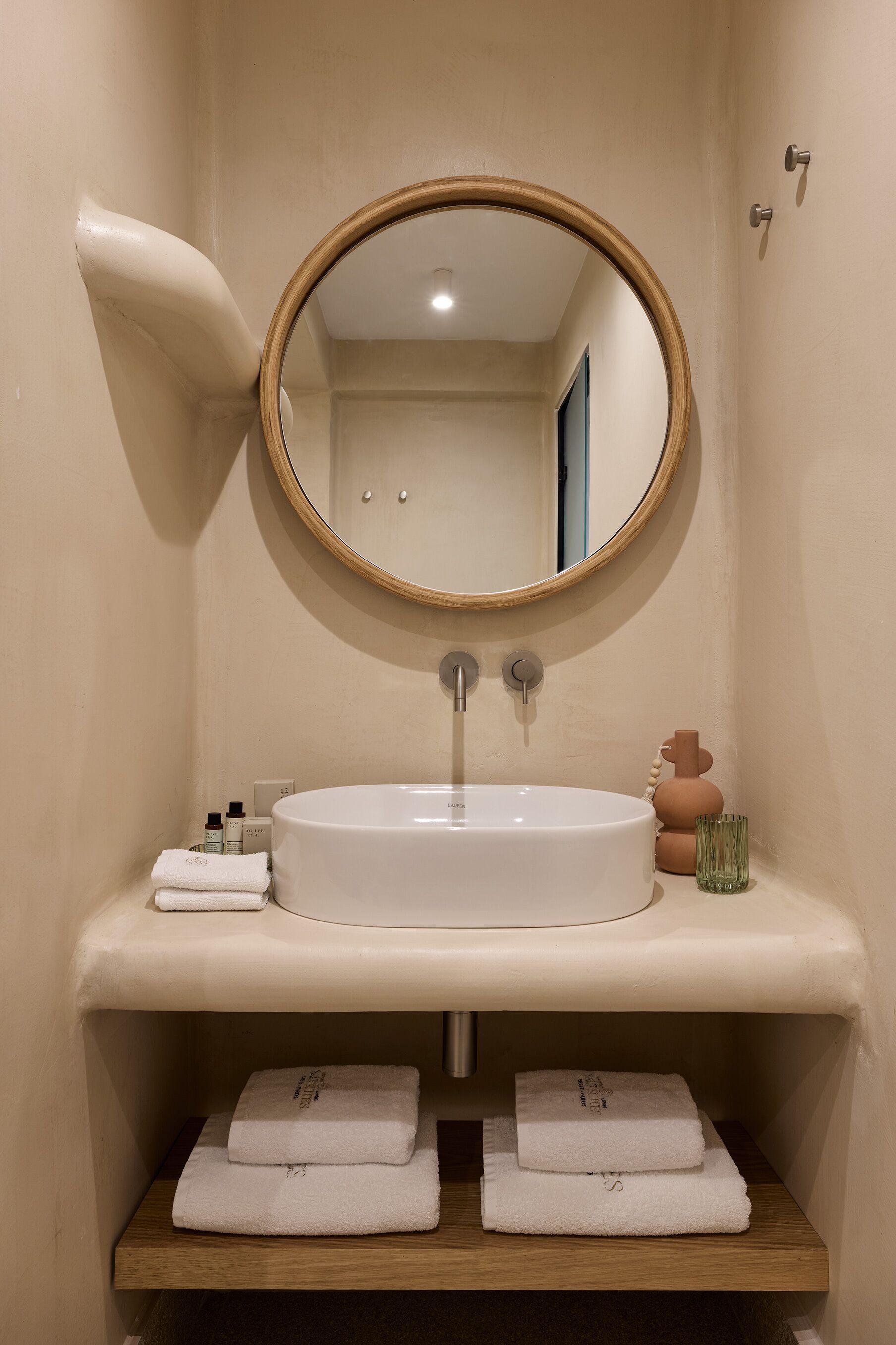 A bathroom with a round mirror, a white sink, and two towel stacks.
