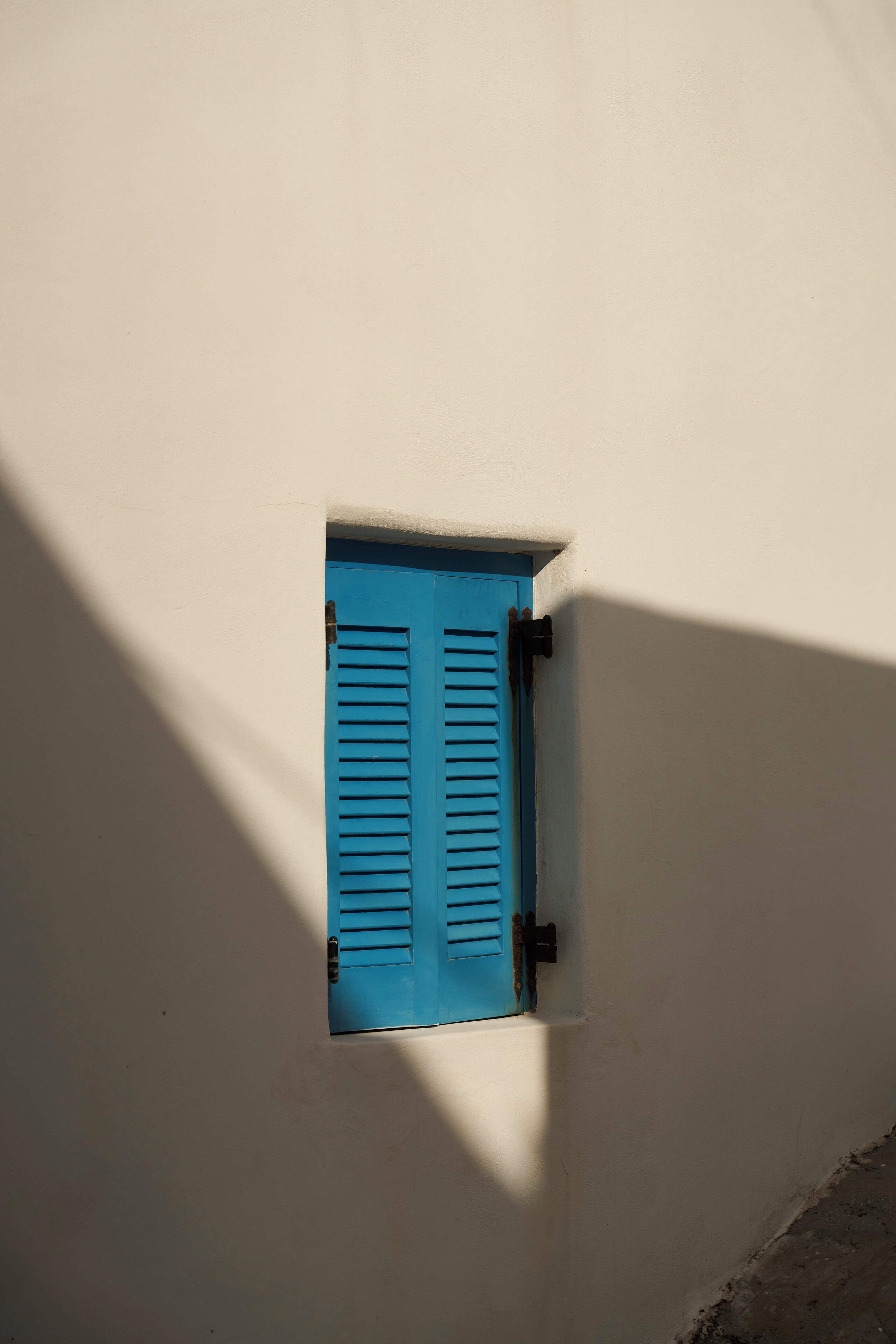 A blue door set in a white wall with a shadow cast on the wall.