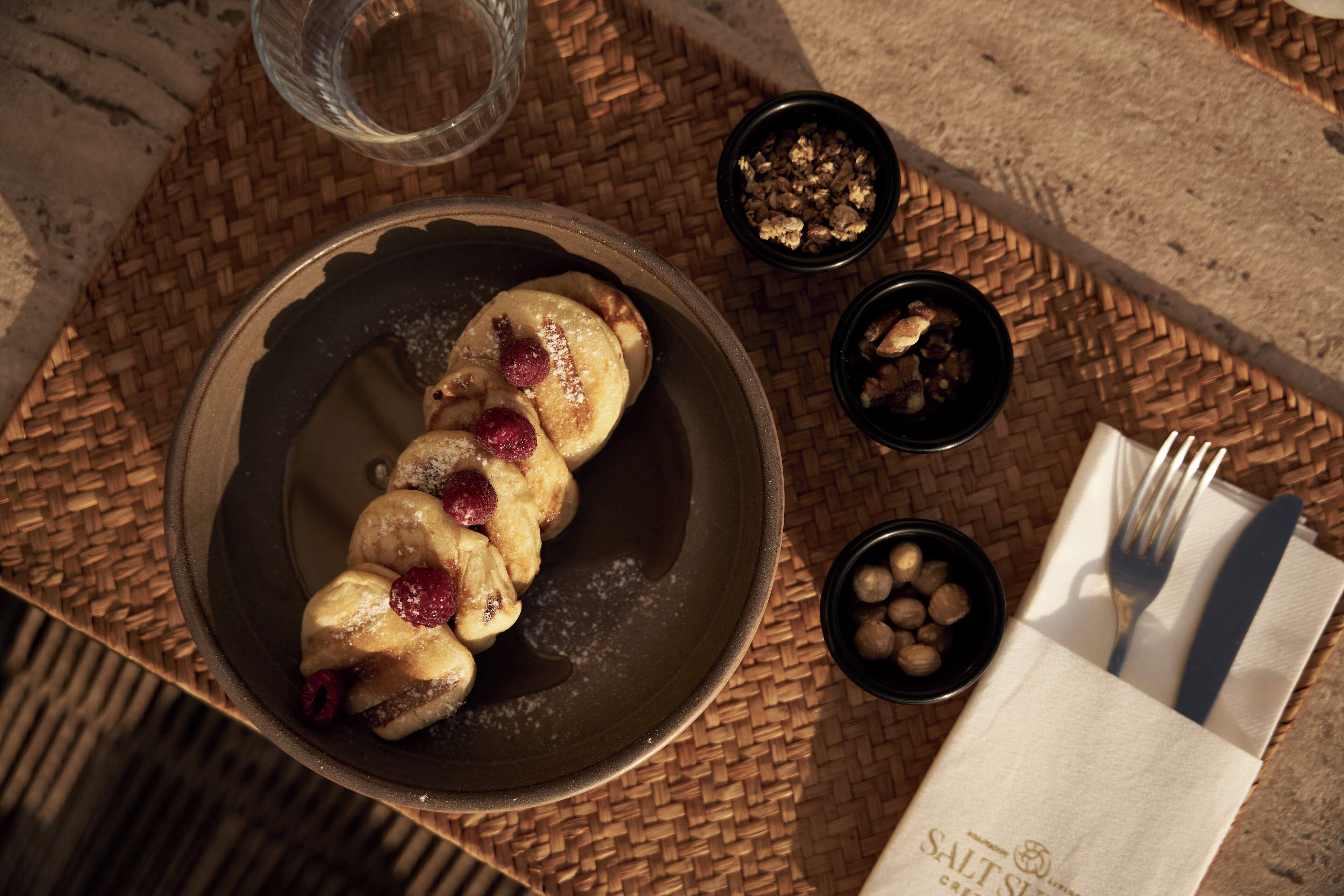 A plate of pastries with berries, a glass of water, and a napkin with cutlery on a woven mat.