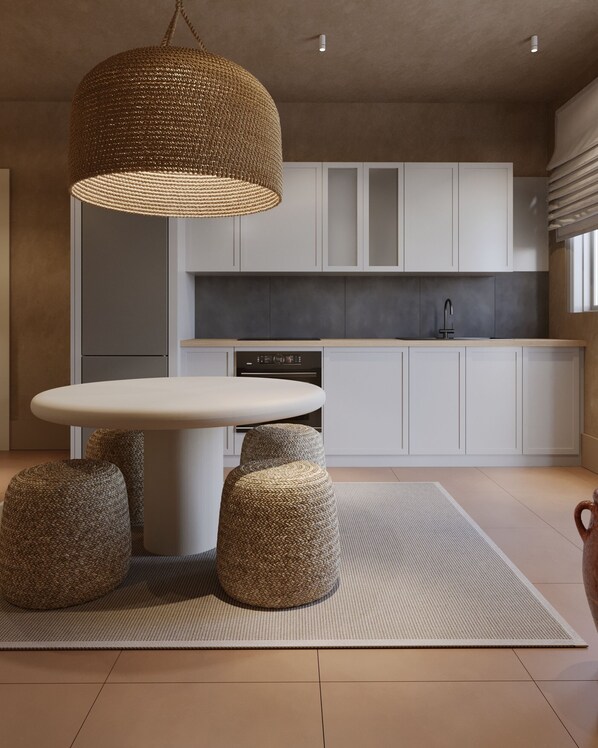 A modern kitchen with white cabinets, a round dining table with stools, and a woven pendant light.