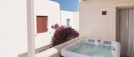 Un jacuzzi sur un balcon aux murs blancs et au plafond en bois.