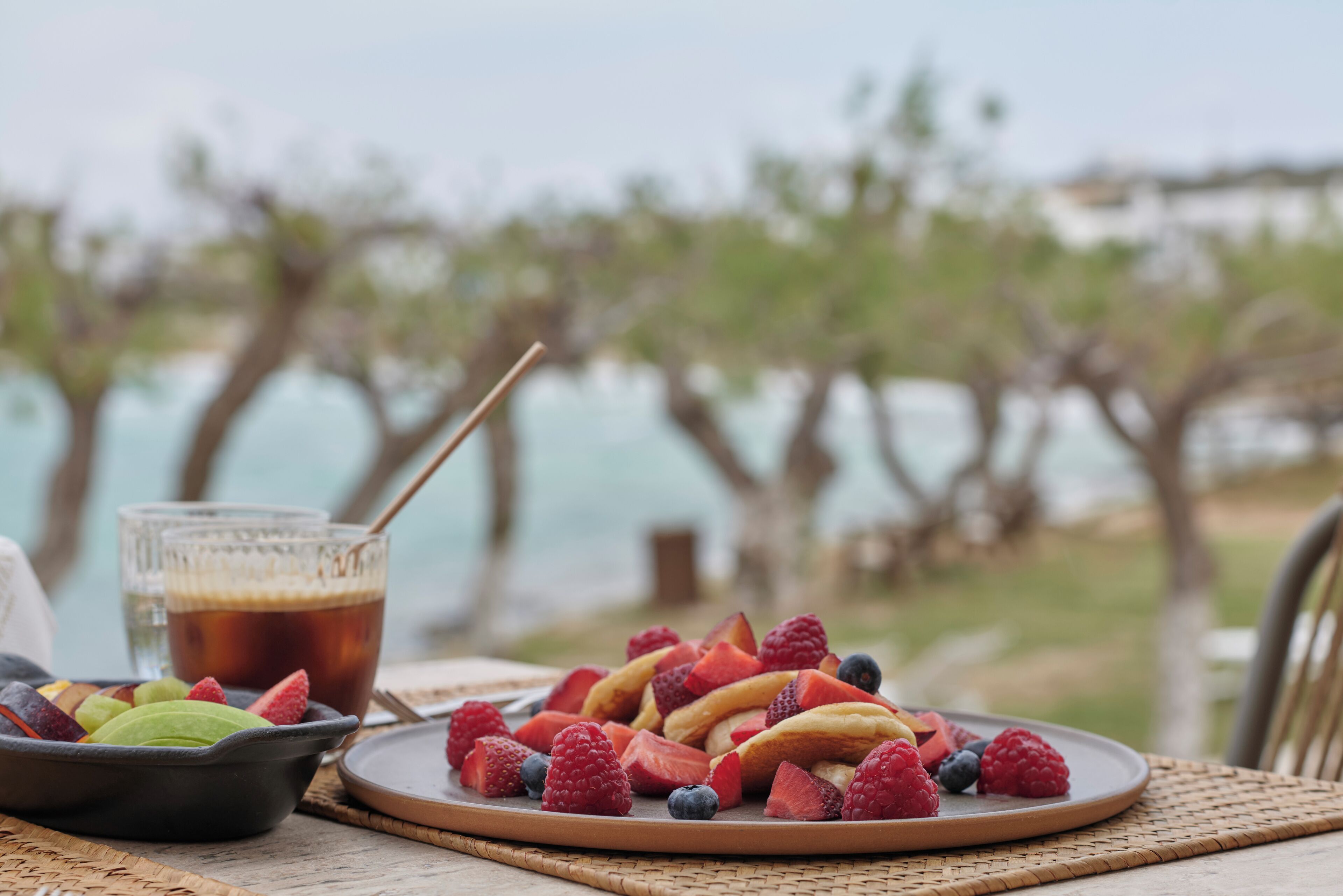 A table with a fruit platter, a glass of iced tea, and a bowl of green apples.