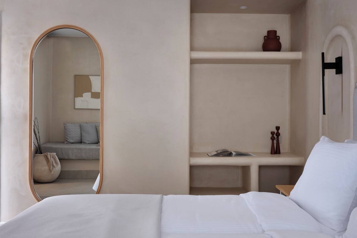 Quarto com cama, espelho, estantes e um pequeno espaço de estar.