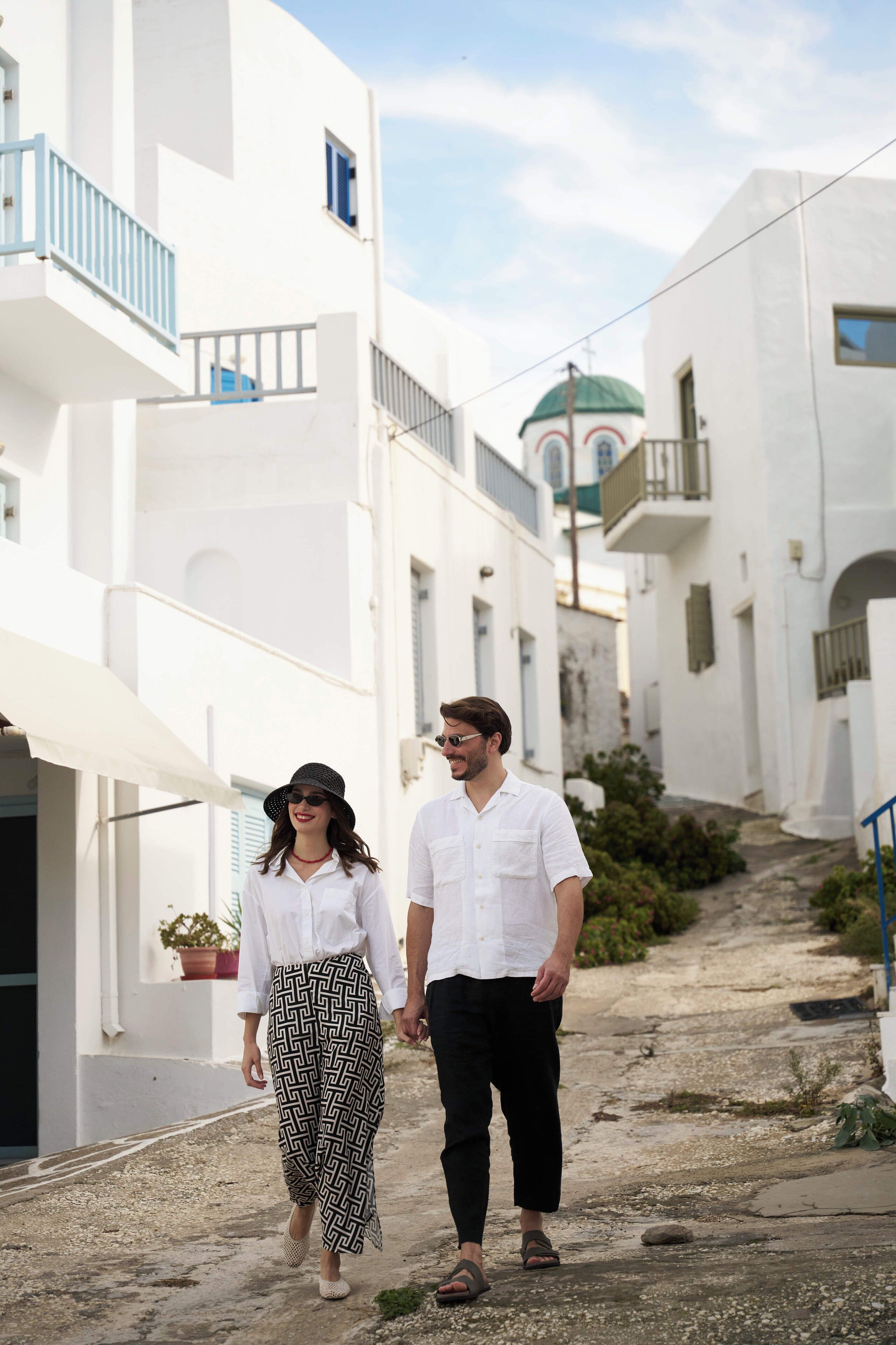 A narrow street with white buildings, a blue railing, and a green dome in the background.