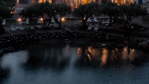 Un hotel frente al mar con varias construcciones, mesas al aire libre junto al agua y ventanas iluminadas.
