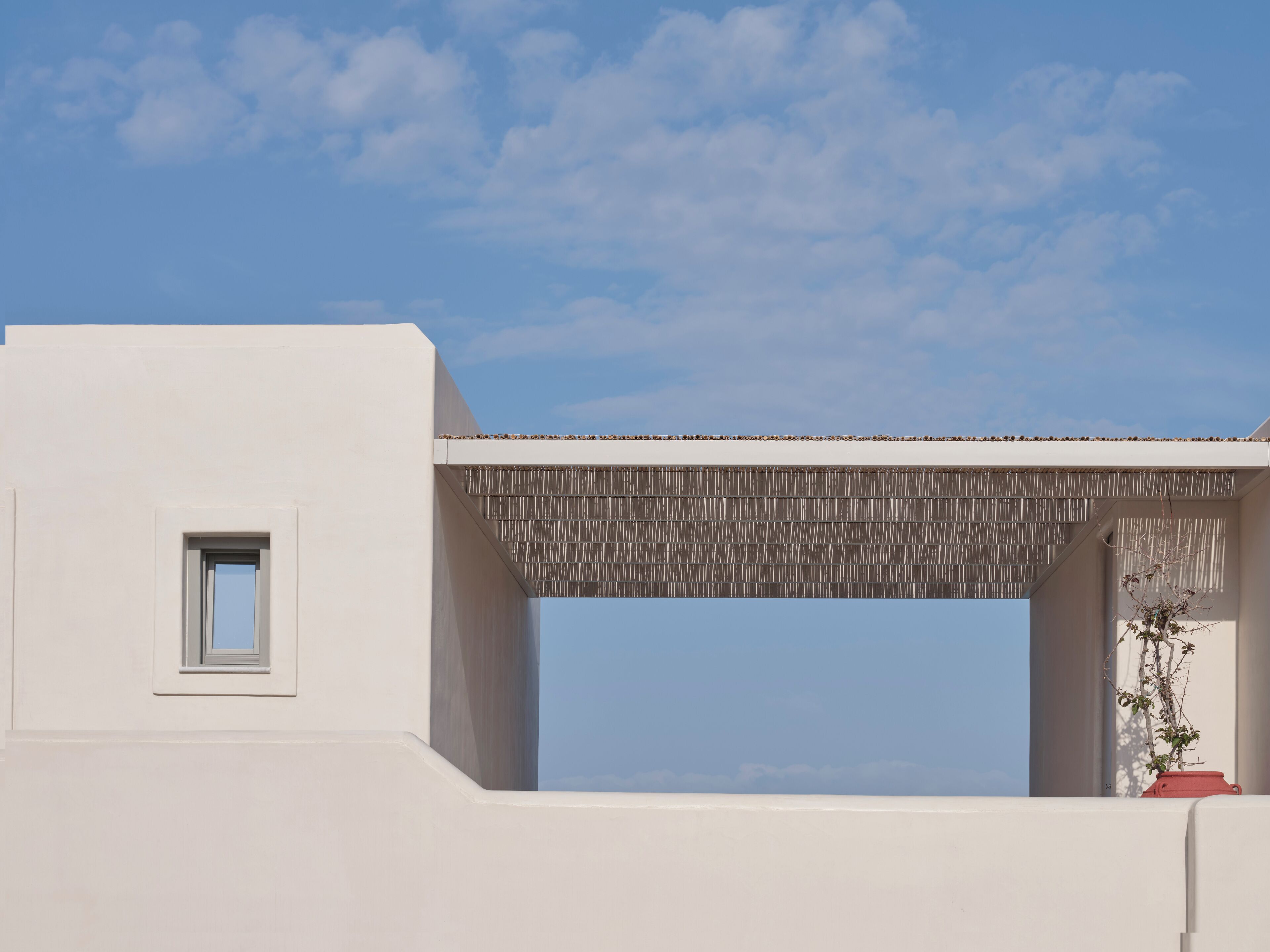 A modern building with a white facade, a small window, and a covered outdoor area with a view of the sky.