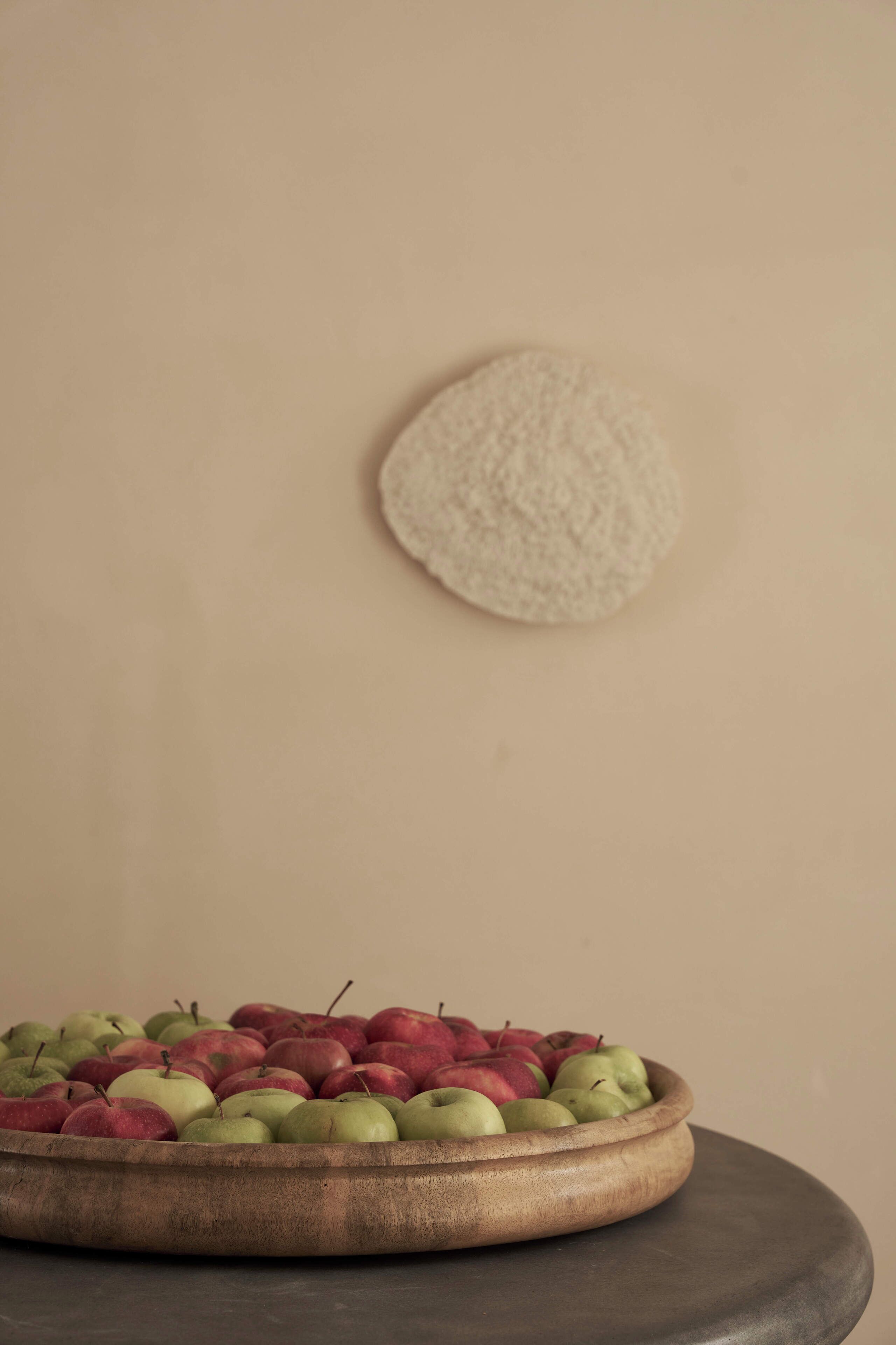 A wooden bowl filled with apples on a table against a plain wall.