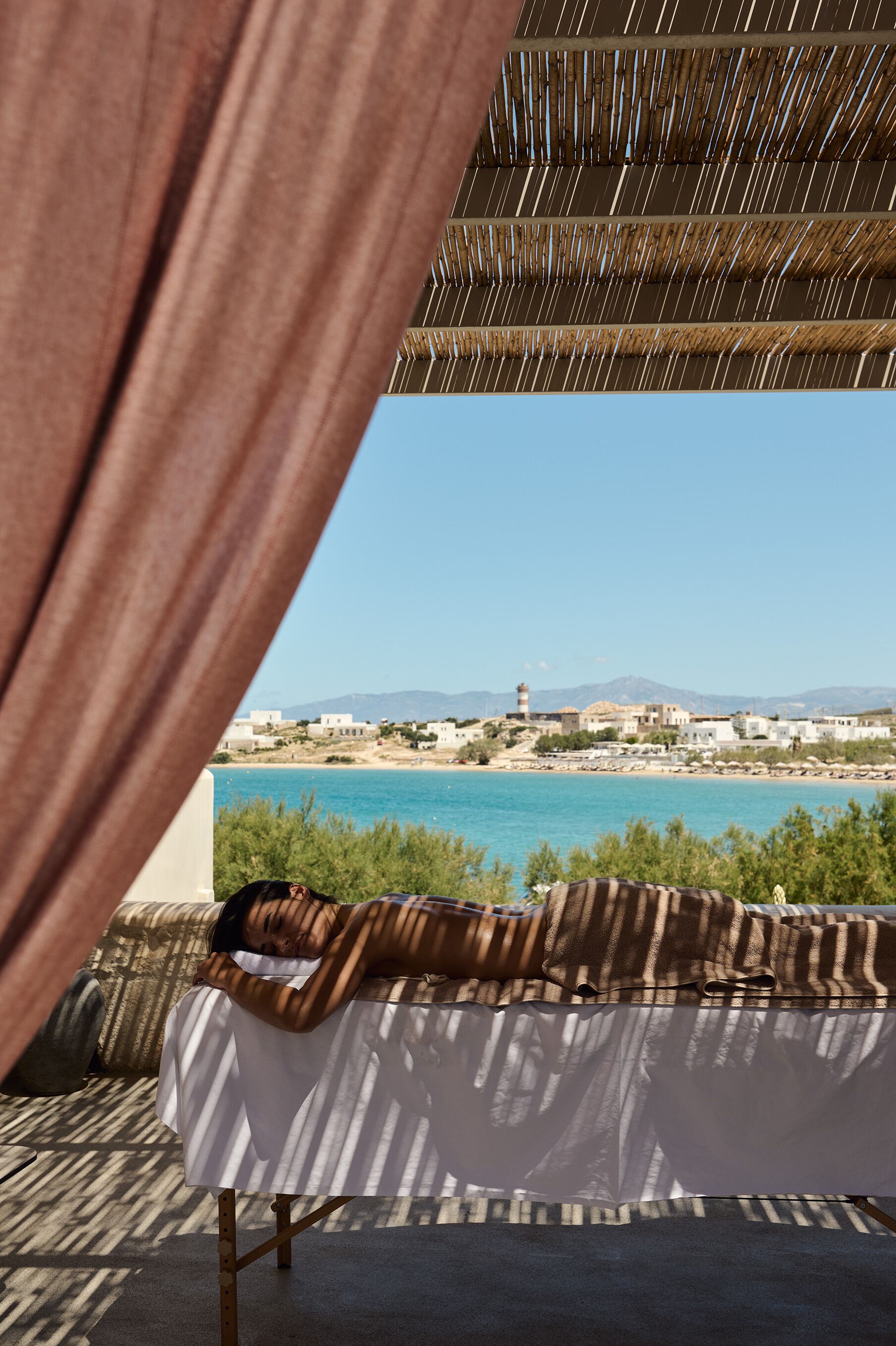 A person lying on a bed with a view of a coastal town and a lighthouse.