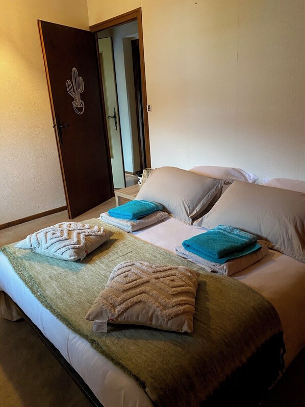 A neatly made bed with a green and white blanket, two blue towels, and decorative pillows.