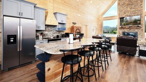 A modern kitchen with a large island, stainless steel appliances, and a stone accent wall. - Brand new gorgeous 5BR cabin with mtn views, game room, hot tub, movie theater! (Sevierville)