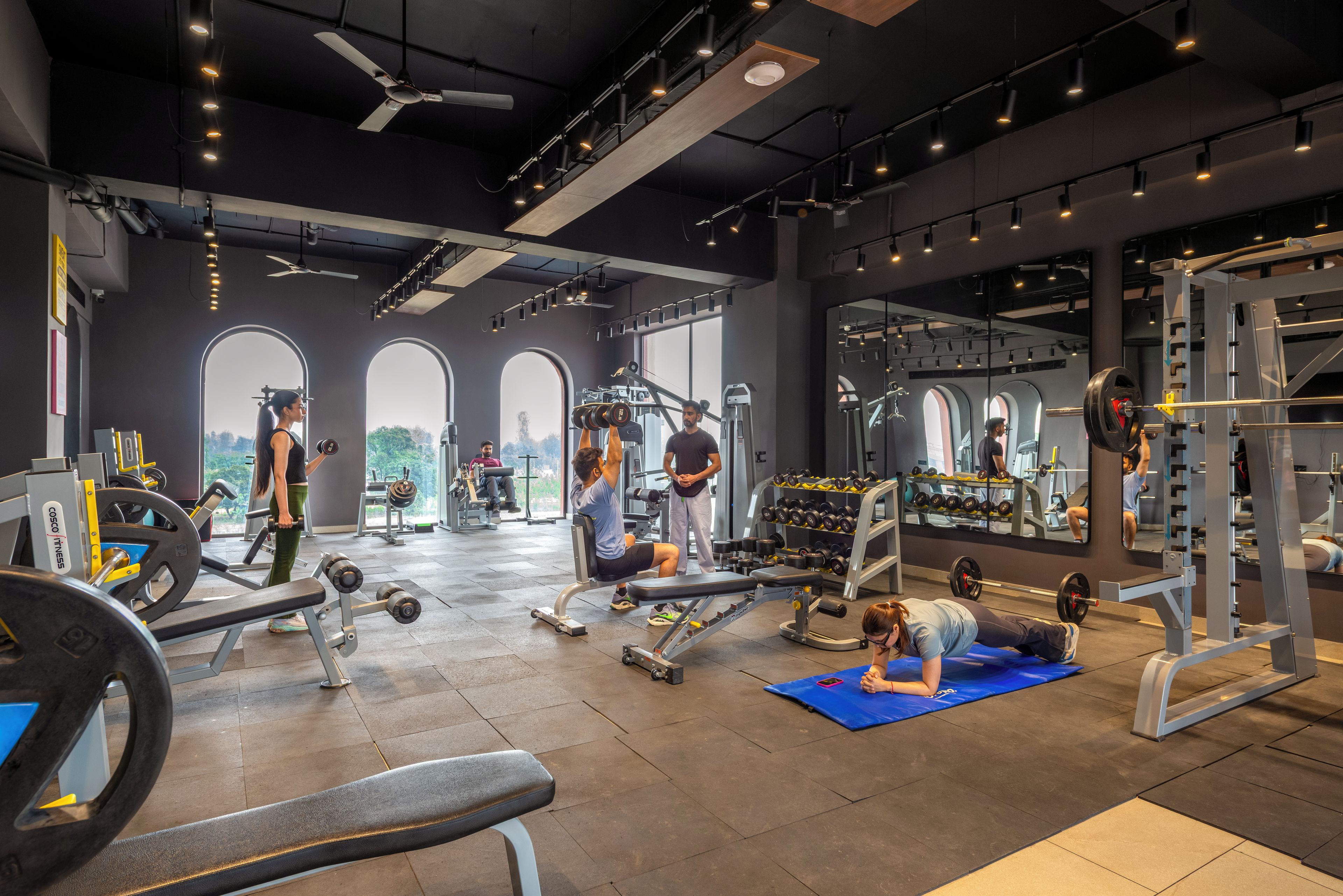 A gym with various exercise equipment, large windows, and a high ceiling.