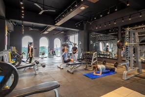 Un gimnasio con diversos equipos de ejercicio, ventanas amplias y un techo alto.