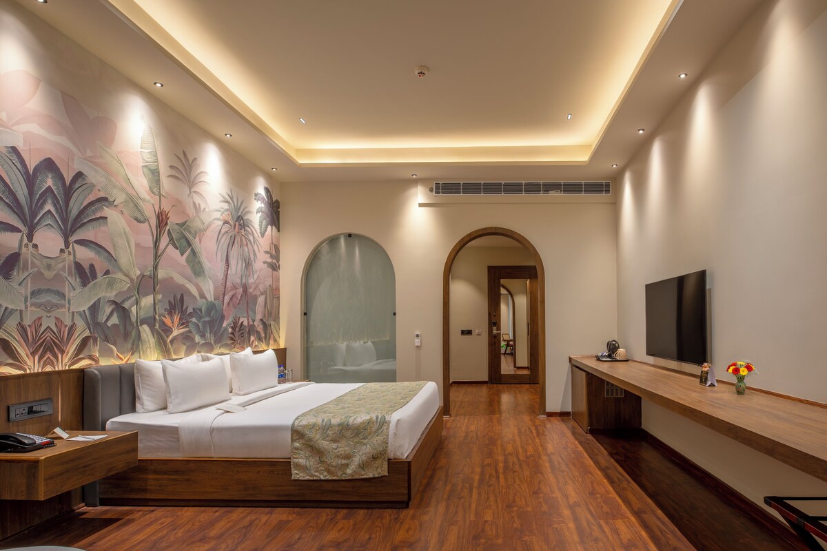 A modern hotel room with a large bed, a TV, a desk, and a mural on the wall.
