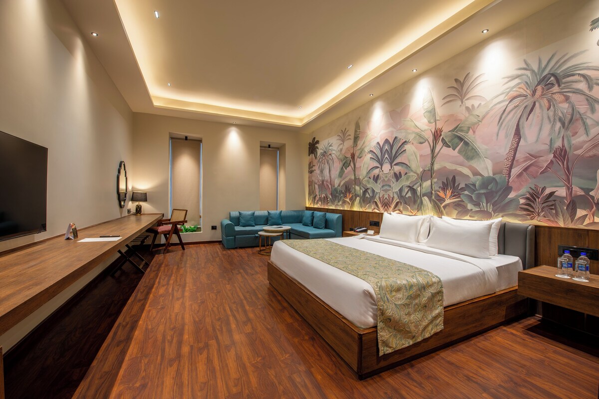 A hotel room with a large bed, a sofa, a desk, and a TV.