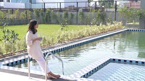 Una piscina con borde a cuadros, rodeada de césped y plantas.