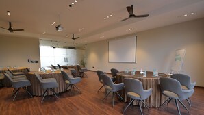 A conference room with multiple tables and chairs, ceiling fans, and a projector screen. - Tree of Life Ganga Dwar, Haridwar (Haridwar)