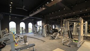 Un gimnasio amplio con diversas máquinas de ejercicio, ventanas grandes y un techo alto.