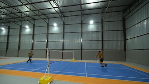 An indoor sports facility with a blue and orange floor, a net, and two people playing a sport. - Tree of Life Ganga Dwar, Haridwar (Haridwar)