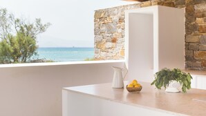 Une cuisine avec un mur en pierre, un réfrigérateur blanc, un pichet, un saladier rempli de citrons et une passoire contenant des herbes aromatiques.