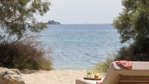 Une vue sur la plage, avec un fauteuil de relaxation, une table avec une boisson et une île au loin.