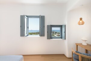Quarto com duas janelas, piso de madeira, cama, cadeira e mesa com abajur.
