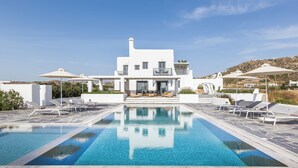 Une villa moderne, blanche, dotée d’une piscine, de chaises longues et de parasols.