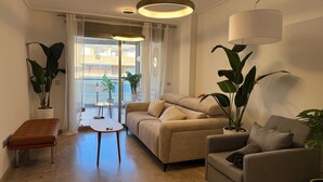Una sala moderna con un sofá color beige, una mesita, un banco y dos plantas grandes en macetas.