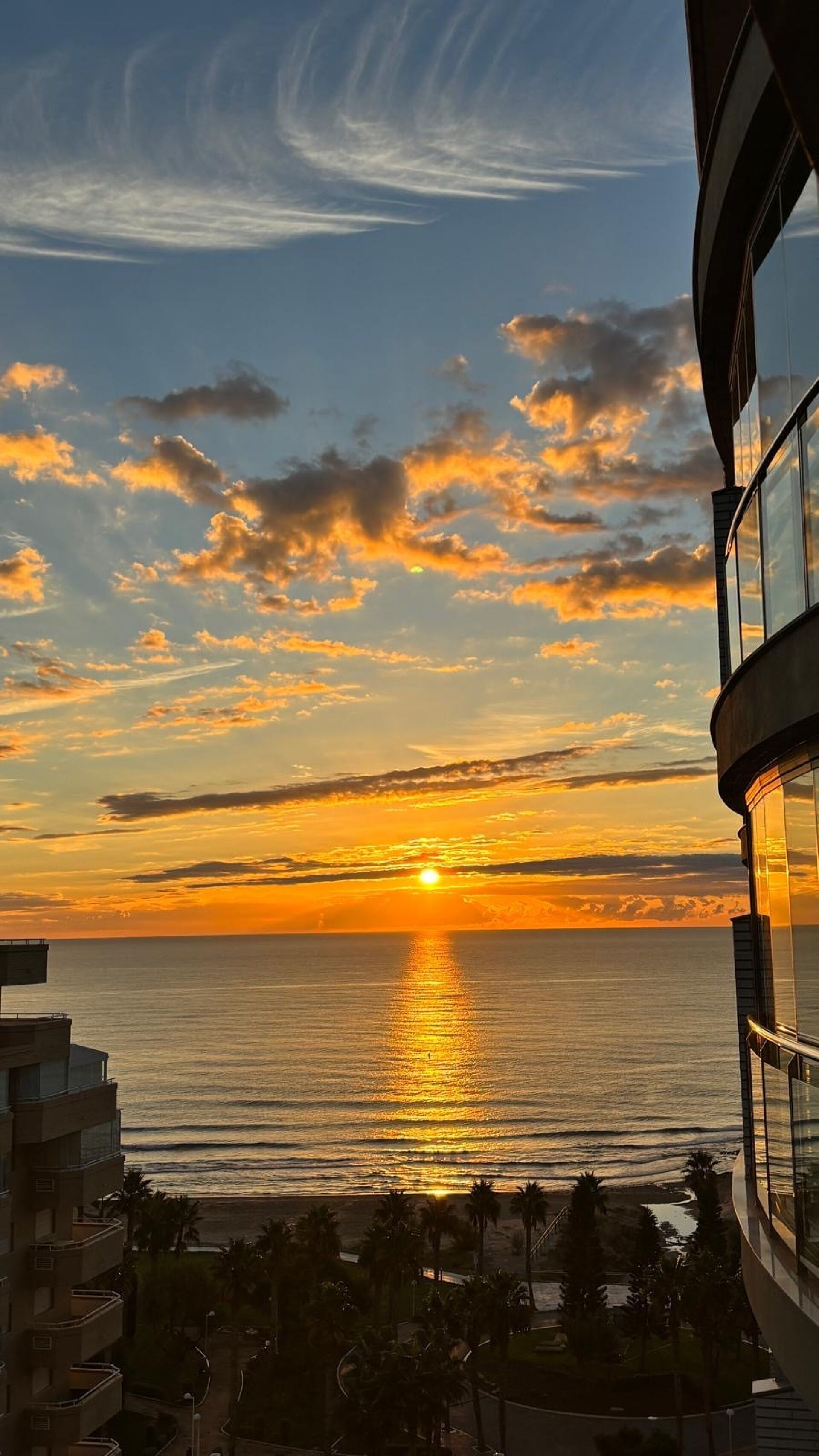 A sunset over the ocean with a view of a modern building with balconies.
