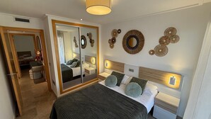 Un dormitorio moderno con un espejo grande, arte decorativo en la pared, una cama con muchas almohadas y lámparas de noche.