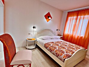 A bedroom with a bed, a chair, a bedside table, and a wall-mounted lamp. - Residenza Delfina (Canale Monterano)