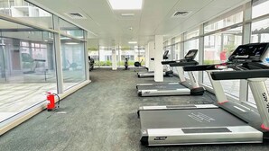 A gym with treadmills, exercise equipment, and large windows offering views of the outside. - Bloomfields Lavish STU in Oasis Masdar (Abu Dhabi)